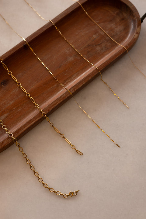 Gold chain on a wooden tray with a neutral background